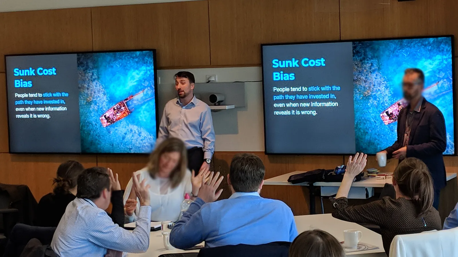 A full room of public servants at the workshop, with a slide on sunk cost bias on screen